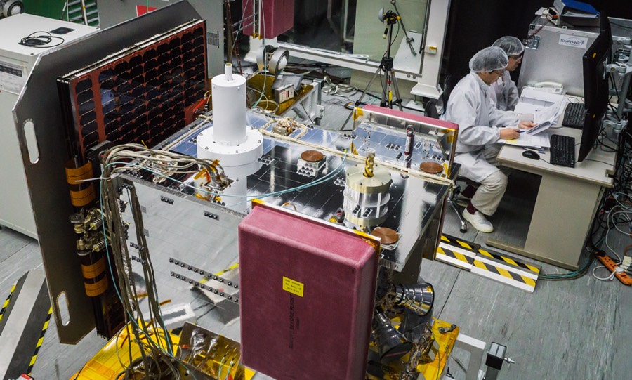 The COSMIC-2 FM2 satellite beside engineers testing it at Taiwan’s National Space Organization; a red rectangular cover protects the radio-occultation hardware.